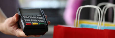 Close-up of person holding terminal for plastic credit card. Cashier machine to withdrawals finance. Nfc technology counter. Colourful packages with stuff. Contactless payment conceptの写真素材
