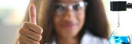 Researcher with microscope and flask holds thumb up. Notable discoveries in the field of medicine conceptの写真素材