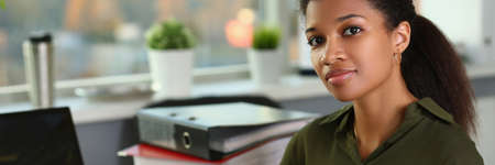 African woman businesswoman sits behind steel worker holds clipboard pen near laptop. Remote work and learning conceptの写真素材