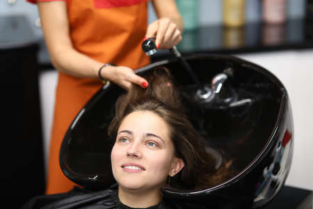 Master washes her hair in sink for client in hairdressing salon. Services of beauty salons and hairdressing salons conceptの写真素材