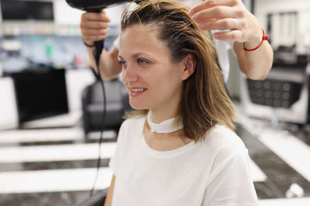 Woman in a beauty salon dry her head with hairdryer. Hair styling training conceptの写真素材