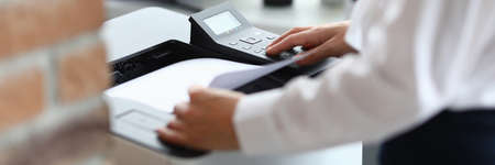 Woman in office prints documents on printer. Scanning documents at workplace conceptの写真素材