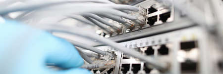 Technician checks the quality of internet connection against background cable hub close-up. Computer...
