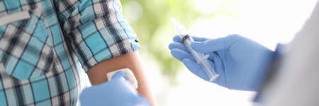 Doctor holding syringe with medicine in hands and wiping patients skin with antiseptic close-up. Vaccine prophylaxis conceptの写真素材