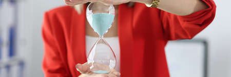 Woman in business suit holding hourglass in her hands in office closeup. Deadline for resolving issues conceptの写真素材