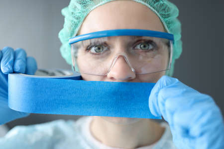 Woman doctor sealing her mouth with blue tape. Medical secrecy conceptの素材 [FY310163986384]