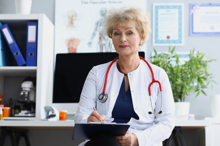 Woman doctor in medical office holds clipboard in her hands. Medical services conceptの写真素材