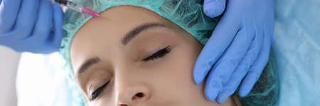 Doctor beautician injects injection into forehead of young woman in beauty salon. Aesthetic medicine skin rejuvenation concept.の写真素材