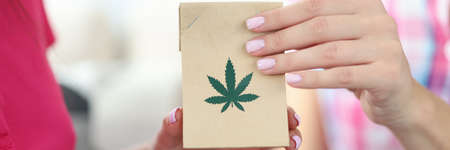 Female hands hold package with hemp leaves close-up. Legal delivery of marijuana narcotic substances concept.の写真素材