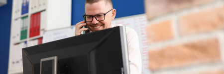 Businessman in office smiling talking on phone and looking at computer screen. Business negotiations...