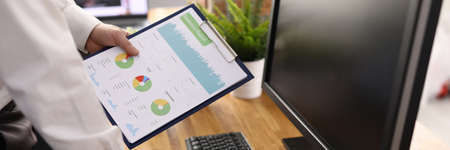 Male hand holds charts with commercial indicators in workplace. Small and medium business...