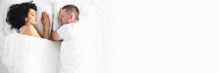 Man and woman on white bed lie with their eyes closed. Intimate relationship in couples conceptの写真素材