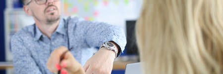 Man in an office points to watch to his employee. Workplace deadlines conceptの写真素材
