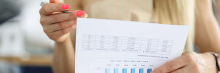 Womans hand holds a pen and document with commercial indicators on chart. Business efficiency...