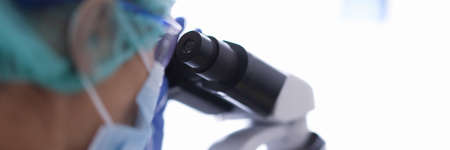Doctor laboratory assistant in goggles and medical mask looks through a microscope. Laboratory research concept conceptの写真素材