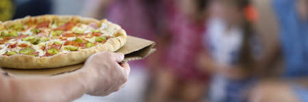 Man delivering cooked homemade hot pizza close-up to family. In background, family wait for italian food.の写真素材