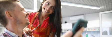 Woman hairdresser smiles and holds hair clipper in her hands and communicates with client. Mozhnoe mens haircuts beauty salon conceptの写真素材