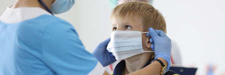 Boy is put on protective medical mask in doctors office. Child health safety in pandemic conceptの写真素材