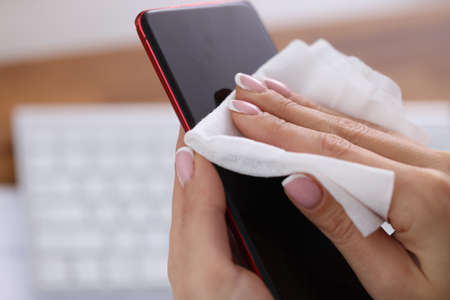 Woman wiping screen of mobile phone with damp cloth closeup. Antiseptic during covid19 pandemic conceptの写真素材