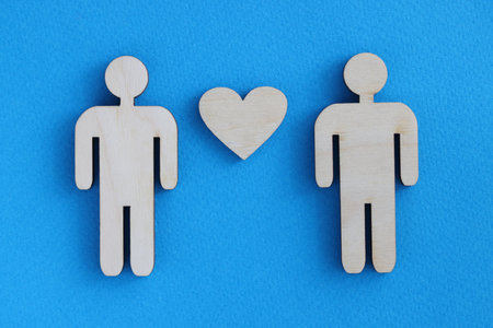 Wooden toy men and heart lying on blue background. Love between men conceptの写真素材