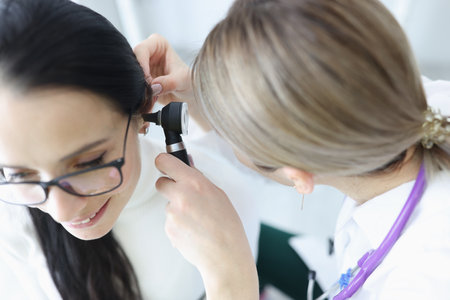 Otorhinolaryngologist doctor examining patients ear with otoscope in clinic. Deafness diagnostics conceptの写真素材