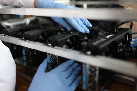 Master in gloves installing video card in mining farm closeup. Repair of computer equipment conceptの写真素材