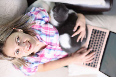 Woman with cat sitting on sofa with laptop top view. Telework conceptの写真素材