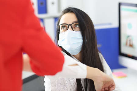 Woman in protective mask greeting each other with her elbows. Security measures during covid19 pandemic conceptの写真素材