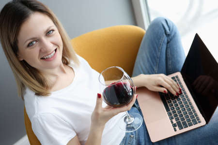 Woman with glass of wine sitting with laptop on her lap. Social media communication concept