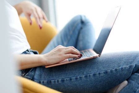 Woman sitting in chair with laptop on her lap closeup. Self isolation concept