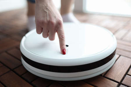 Woman pushing button in robot vacuum cleaner closeup. Repair of household appliances conceptの写真素材