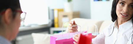 Close-up of cute businesslady giving present to friend. Lady sitting on sofa in office. Female...