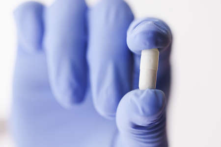 White medical capsule is held by doctor in a gloveの写真素材