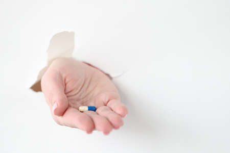 Hand pulling out medicine capsule from torn paperの写真素材