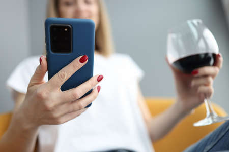 Woman looks into smartphone and holds glass of wine in her handの写真素材