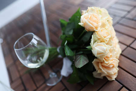 Bouquet of roses lying on wooden floor near glass of white wine closeupの写真素材