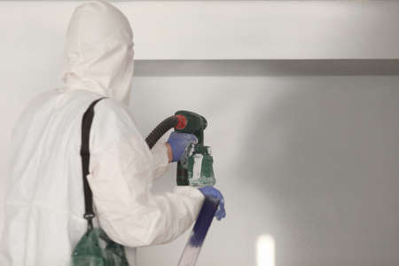 Master painter in white suit paints wall with a spray gunの写真素材