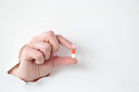 Female hand holds medical pill through hole through white paperの写真素材