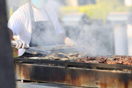 Chef prepares meat on grill in open air