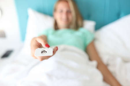 Woman lying in bed presses buttons on remote control