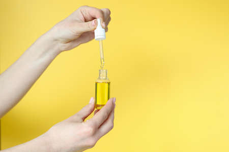 Woman holding cosmetic oil in her hands on yellow background closeupの写真素材