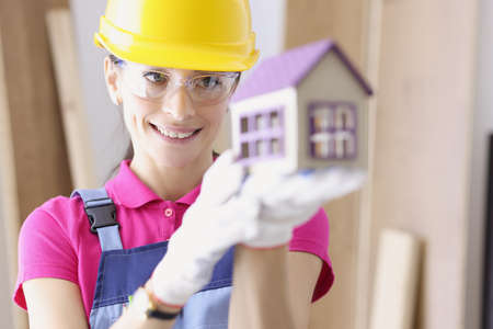 Smiling woman builder holding house in her hands