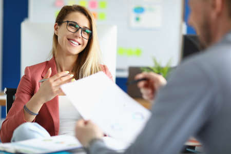 Smiling businesswoman with glasses communicating with colleague in officeの写真素材