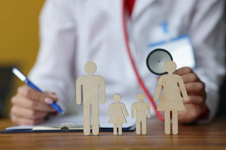 Doctor writing in medical documents and holding stethoscope in front of toy men closeupの写真素材