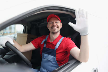 Smiling courier driver in car cab waving his hand in greeting