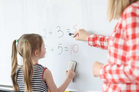 Little girl and teacher solving math equations on blackboardの写真素材