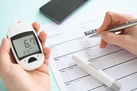 Patient holding glucometer and recording data in diary closeup