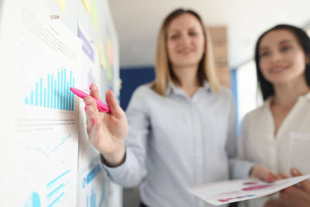 Business women standing at blackboard and showing pen on chart closeupの写真素材