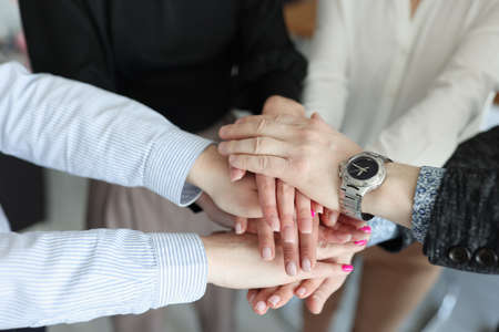 Closeup of many folded hands of businessmen in office
