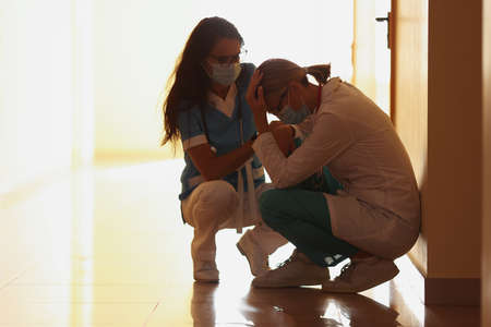 Tired doctors in protective medical mask sit on corridorの写真素材